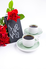 A bouquet of red roses and two cups of coffee on a white background. Gift and romantic breakfast. The concept of Valentine's Day and March 8 in Russia. Copy space.