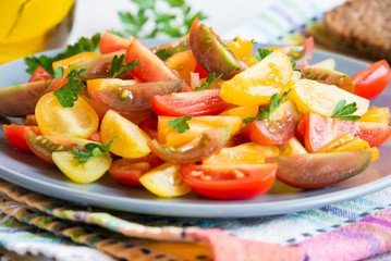 Fresh vegetable salad of mixed tomatoes of different colors. Red, yellow and brown tomatoes cut on plate