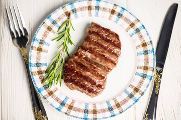 medium grilled beef steak grilled on a plate with fork and knife