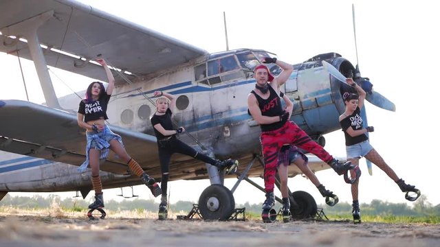 Group training kangoo. Coach with four young sporty women doing fitness exercises with kangoo shoes on an abandoned airfield, against the background of an old airplane.