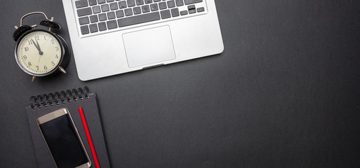 Computer laptop and alarm clock on black color office desk, top view