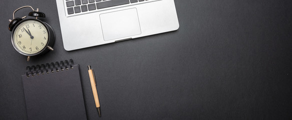 Computer laptop and alarm clock on black color office desk, top view