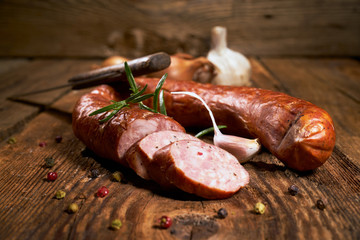 Smoked sausage on a wooden rustic table with the addition of fresh aromatic herbs and spices, natural product, produced by traditional methods