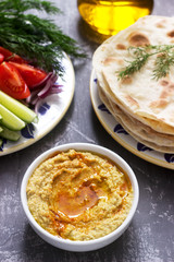 Vegan food, homemade hummus with flatbread, vegetables and olive oil on a concrete background.