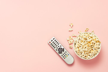 A bowl of popcorn and a TV remote on a pink background. The concept of watching TV, film, TV series, sports, shows. Flat lay, top view