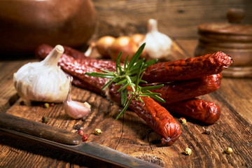 Smoked sausage on a wooden rustic table with the addition of fresh aromatic herbs and spices,...