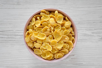 Corn flakes in a pink bowl for breakfast on a white wooden table, top view. Flat lay, overhead, from above. Close-up.