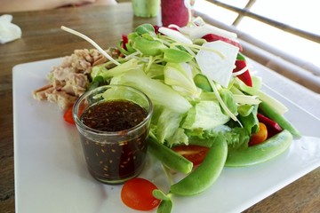 Top view of tuna salad with fresh sunflower sprout, tomato, apple sliced, peas and salad dressing made from sesame oil on white plate, healthy food concept