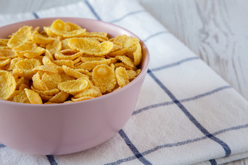 Corn flakes in a pink bowl for breakfast over white wooden background, side view. Copy space.