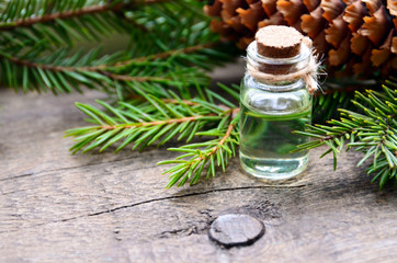 Fir essential oil in a glass bottle and green coniferous tree branches with cones on old wooden table.Spruce aroma oil for spa,aromatherapy and bodycare.Selective focus.