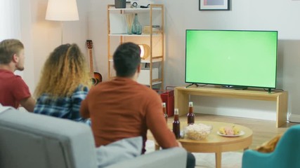 Three Sports Fans Sitting on a Couch in the Living Room Watch Green Chroma Key Screen TV Important Match, Using Horns, Having Fun and Cheering For their Team. - Powered by Adobe