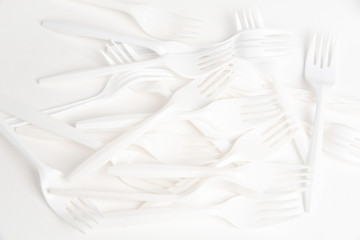 A bunch of disposable single-use white plastic forks set on a seamless white paper background.
