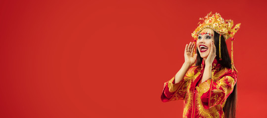 Chinese traditional graceful woman shouting at studio over red background. Beautiful girl wearing national costume. Chinese New Year, elegance, grace, performer, performance, dance, actress, dress