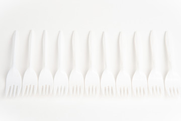 A bunch of disposable single-use white plastic forks set on a seamless white paper background.