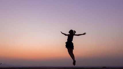 silhouette of woman jumping and free at sunset