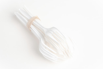 A bunch of disposable single-use white plastic forks set on a seamless white paper background.