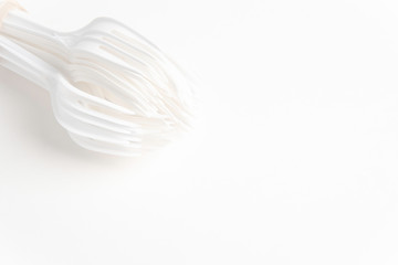 A bunch of disposable single-use white plastic forks set on a seamless white paper background.