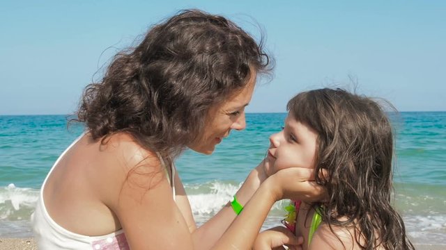 Mother kissing daughter on beach. Mom kisses her little daughter against the background of the sea.