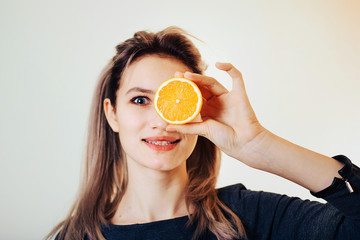 Portrait of an attractive girl covering one eye with a slice of orange.