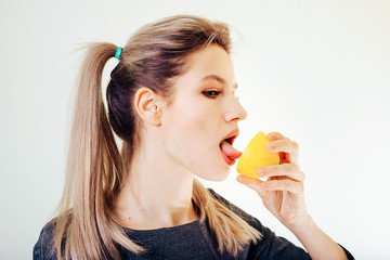 An attractive girl holds a lemon in her hand and licks it.