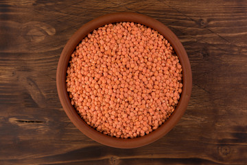 Red lentils in clay plate on wooden table background