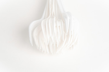 A bunch of disposable single-use white plastic forks set on a seamless white paper background.