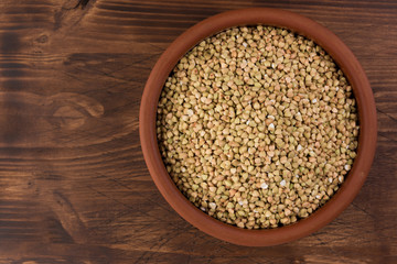 Natural fresh green buckwheat in clay bowl on wooden background. Top view