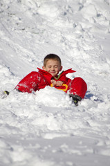 Fototapeta na wymiar vacances d'hiver - enfant en combinaison rouge faisant de la luge