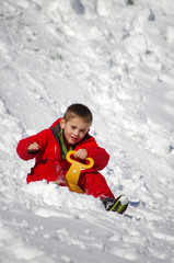 Fototapeta na wymiar vacances d'hiver - enfant faisant de la luge en combinaison rouge