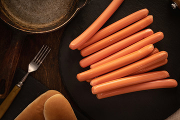 Top view of fresh sausages for hot dogs on a dark background with buns.