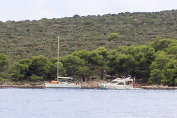 Fototapeta na wymiar A modern sailing yacht is anchored in a bay. People bathe in the sea. Active rest on the Adriatic Sea of the Mediterranean region. Dalmatian riviera of Croatia. Prestigious and rich lifestyle