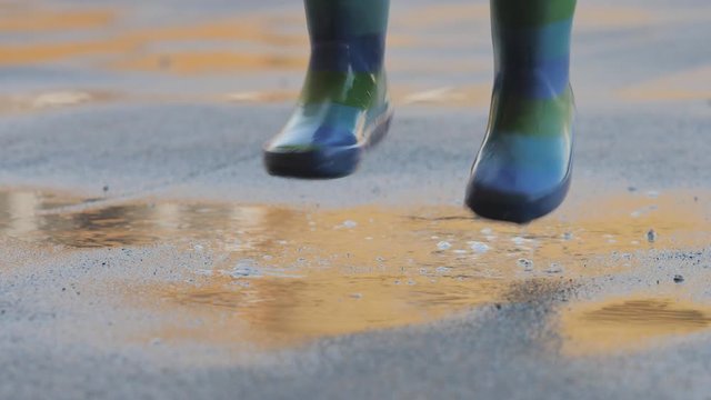 Detail of child rubber boots jumping on puddle, childhood care free, slow motion