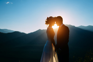 Happy wedding couple staying over the beautiful landscape with mountains during sunset