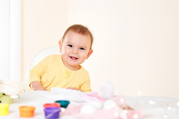 Baby girl sitting at the table and painting holiday easter eggs smiling happy childhood concept