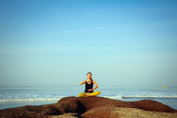 Beautiful young woman practicing yoga and stretching exercises at the summer ocean beach
