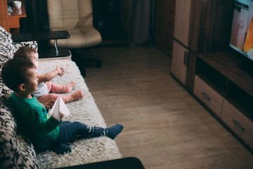 little girl and brother with remote on the couch watching TV on their own