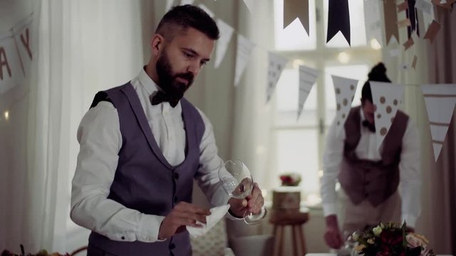 Two men with bows and vests setting a table for an indoor party.