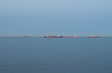 Minimal landscape with ships in the roadstead at calm sea and blue sky background
