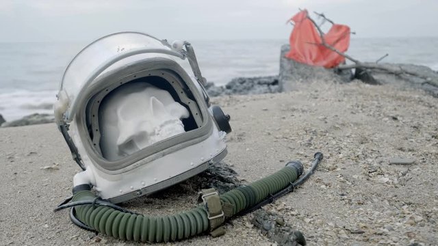 The head of a dead cosmonaut lies on the sand by the sea. Astronaut crashed on his spaceship. Cloudy weather, the wind blows