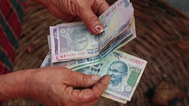 Close up of Poor elderly Indian/Asian woman counting five hundred paper Indian money rupees over her empty vegetable basket. concept of making money in Agriculture