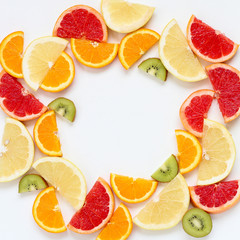 Flat lay of sliced fruits - kiwi, orange and grapefruits - arranged in a circle, copy space in the middle