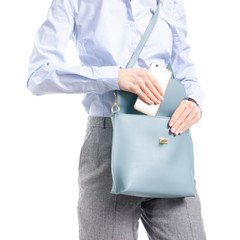 Woman in gray pants and blue shirt put smartphone in blue bag macro on white background isolation