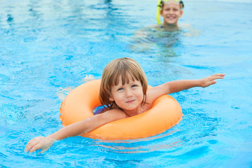 Fototapeta na wymiar Cute little boy swimming in pool with inflatable ring on summer vacation