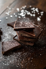 Bitter Chocolate Pieces with Sea Salt on Dark Wooden Surface.