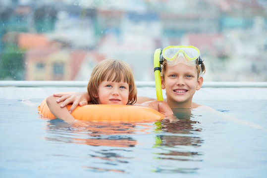 Happy child in snorkel swimming in pool with his brother in inflatable ring