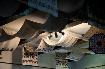 Handmade embroidery. Ceiling drapery with embroidered towels. Decorative old ceiling with drapes. Vintage or retro interior room design. Wood beam ceiling with draped textile and light fixtures