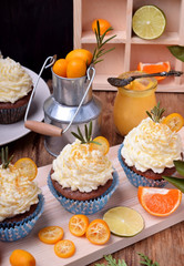 Cupcakes topped with butter cream, slices of kumquat and rosemary surrounded by fruits