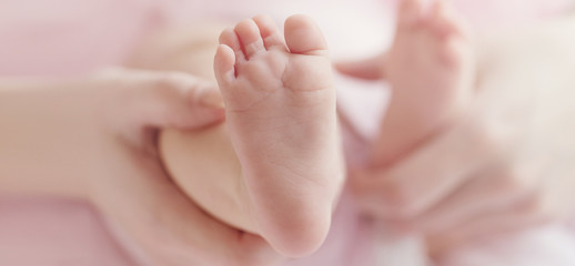 Closeup of mother hands holding cute tiny baby feet, showing baby foot. Pink Background. Horizontal.