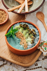 Spirulina Acia bowl with toppings of candied pumpkin seeds, kiwi fruit, bee pollen and fresh mint, on a brown wooden background