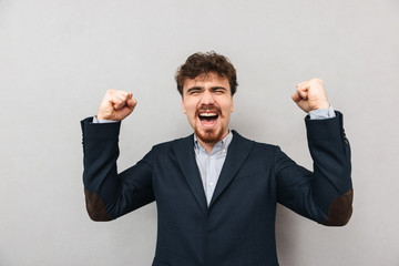 Handsome young business man isolated over grey wall background make winner gesture.